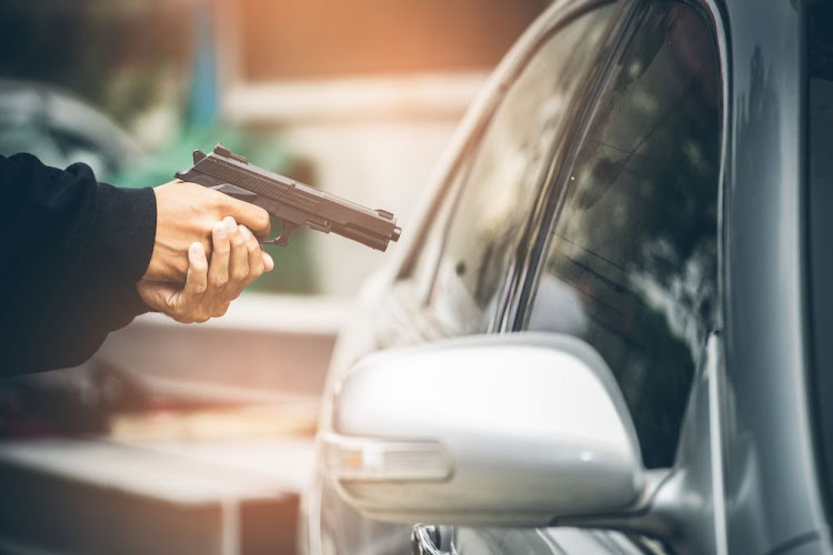 A robber dressed in black pointing a gun at a driver in a car. Car thief concept.