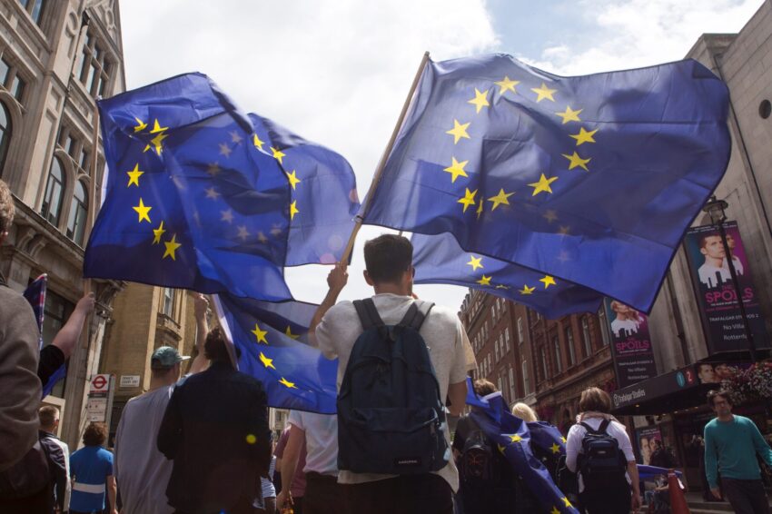 Manifestantes a erguerem bandeiras da UE. Crédito: Freepik