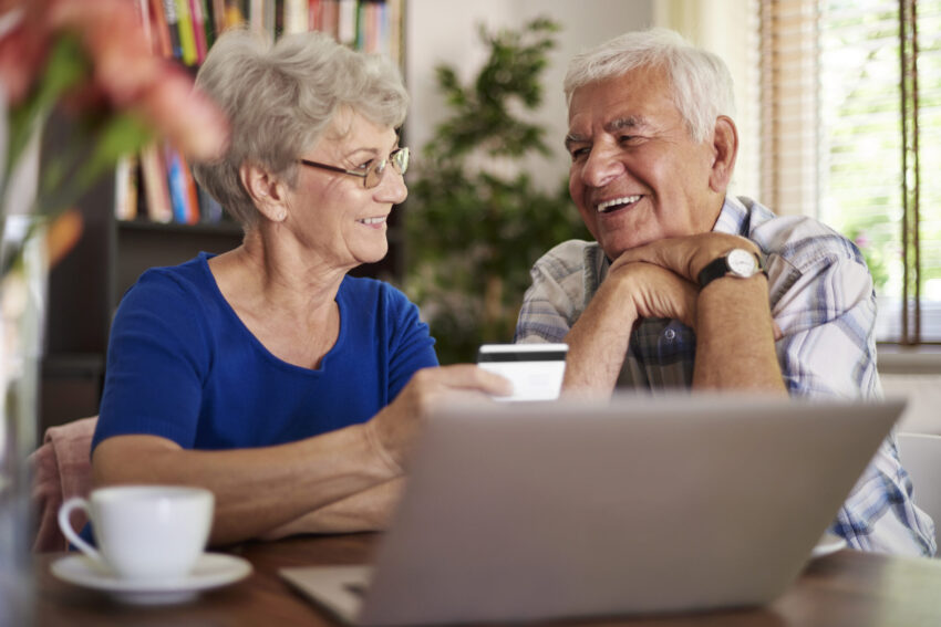 Casal de reformados sorridente em frente ao computador. Crédito: Freepik