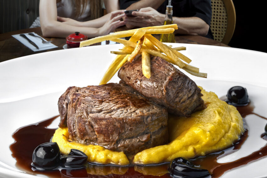 Prato com duas postas de carnes e batatas fritas no topo. Crédito: Freepik