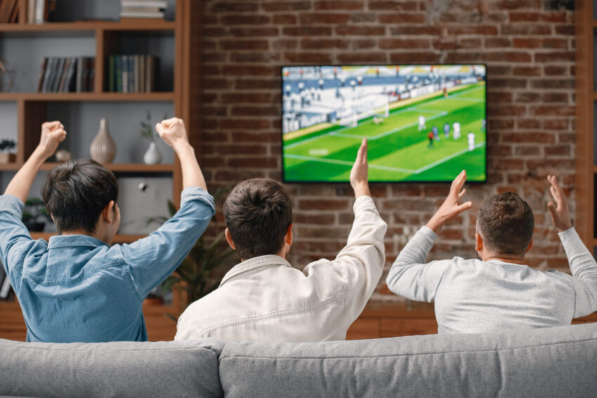 Três homens de costas no sofá a ver um jogo de futebol. Crédito: Freepik
