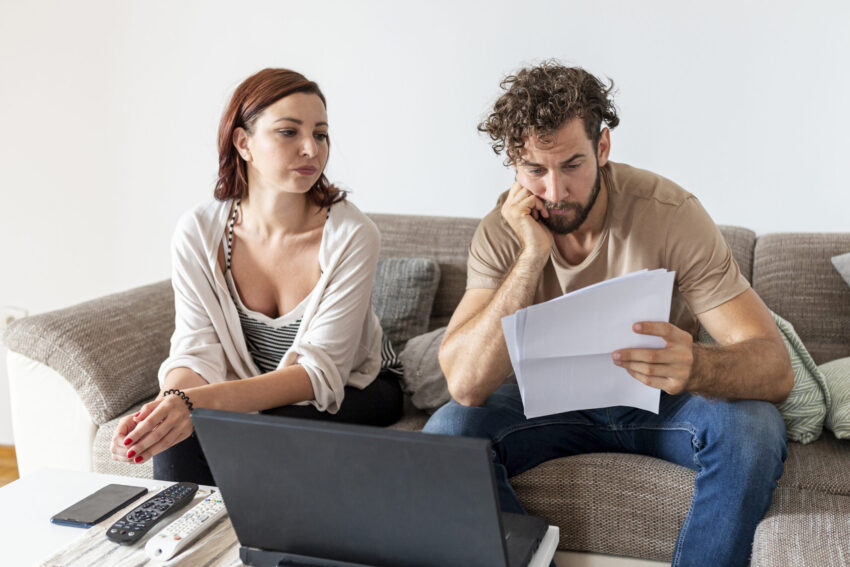 Homem e mulher sentados num sofá a olhar para uma folha de papel. Crédito: Freepik