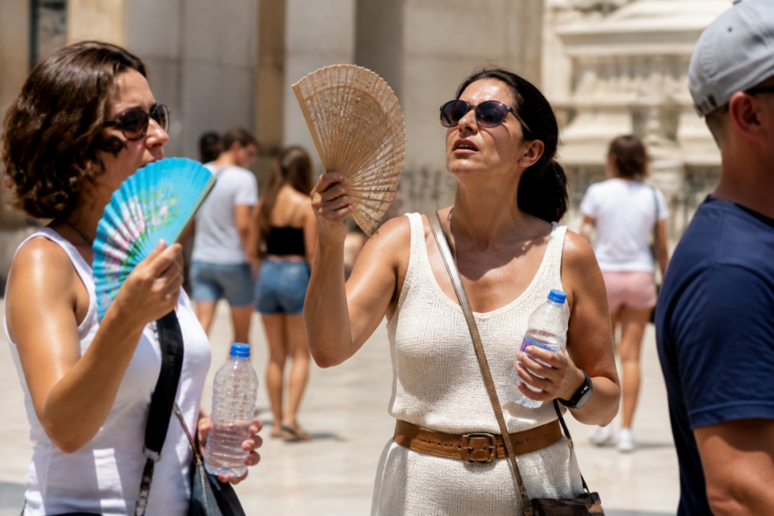 Mulheres abanam leques devido ao calor. Crédito: Magnific AI